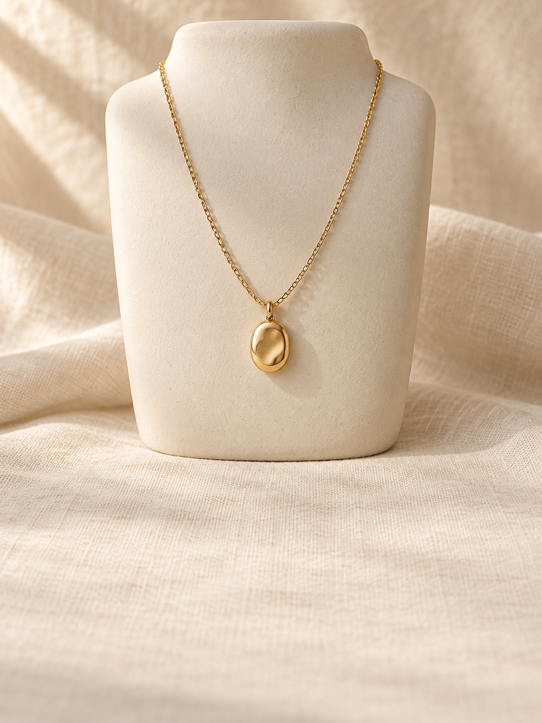 Gold-tone oval pendant on an ivory necklace display